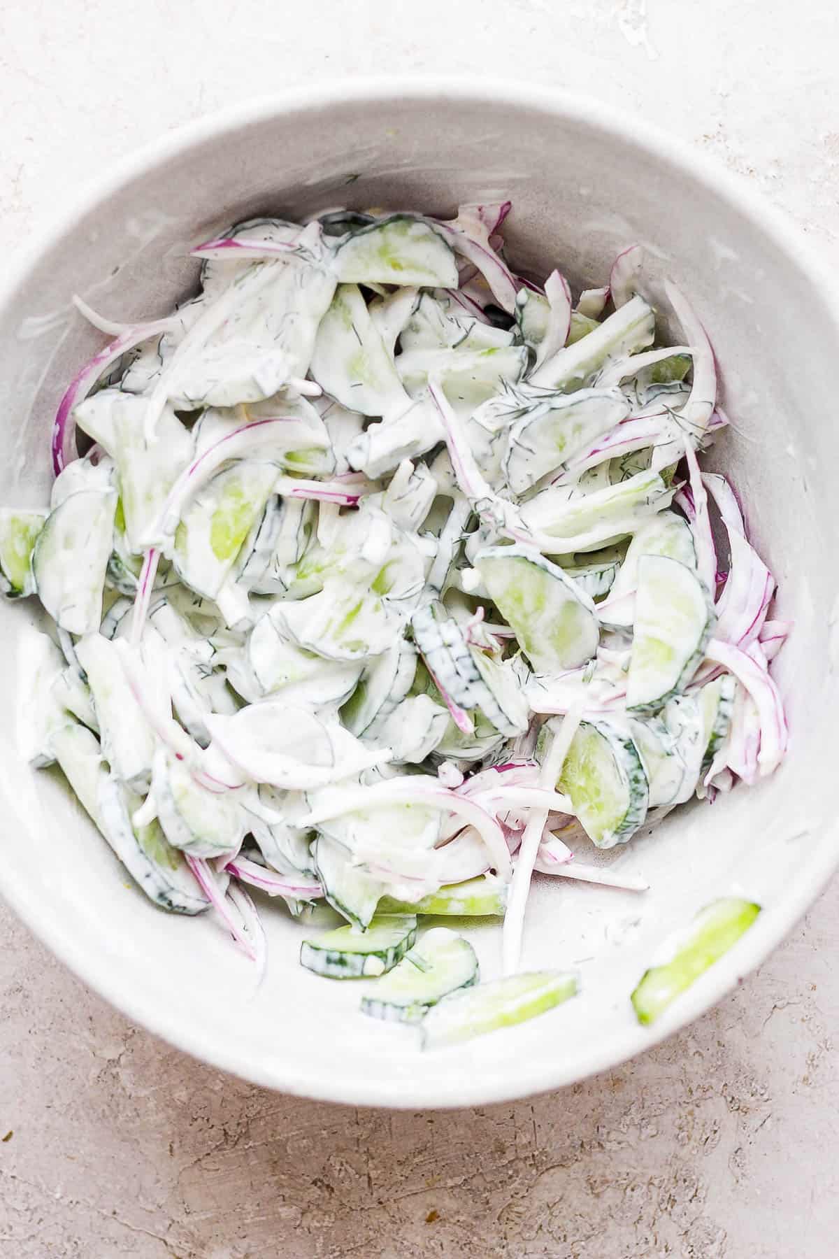 All of the cream cucumber salad ingredients tossed together in the large bowl.