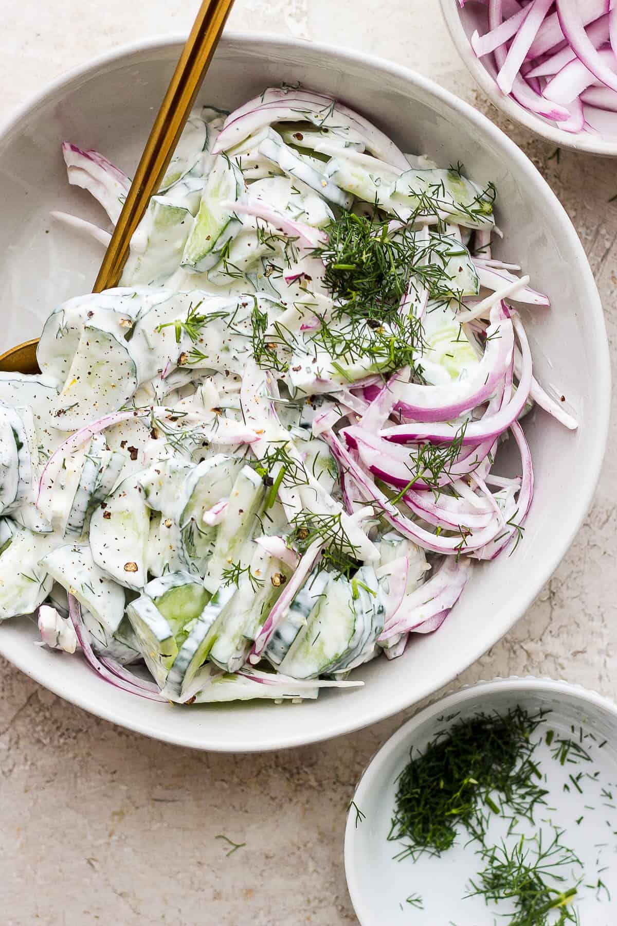A bowl of creamy cucumber salad in a bowl with a spoon inserted into it.