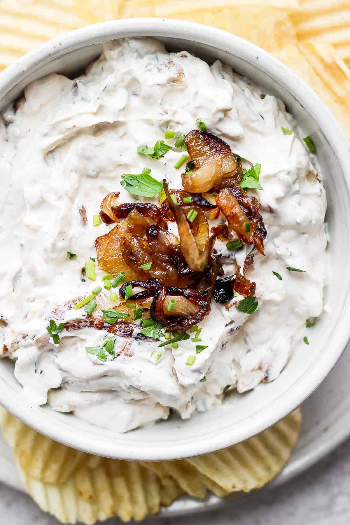 French onion dip in a bowl with some fresh herbs and caramelized onions as garnish.