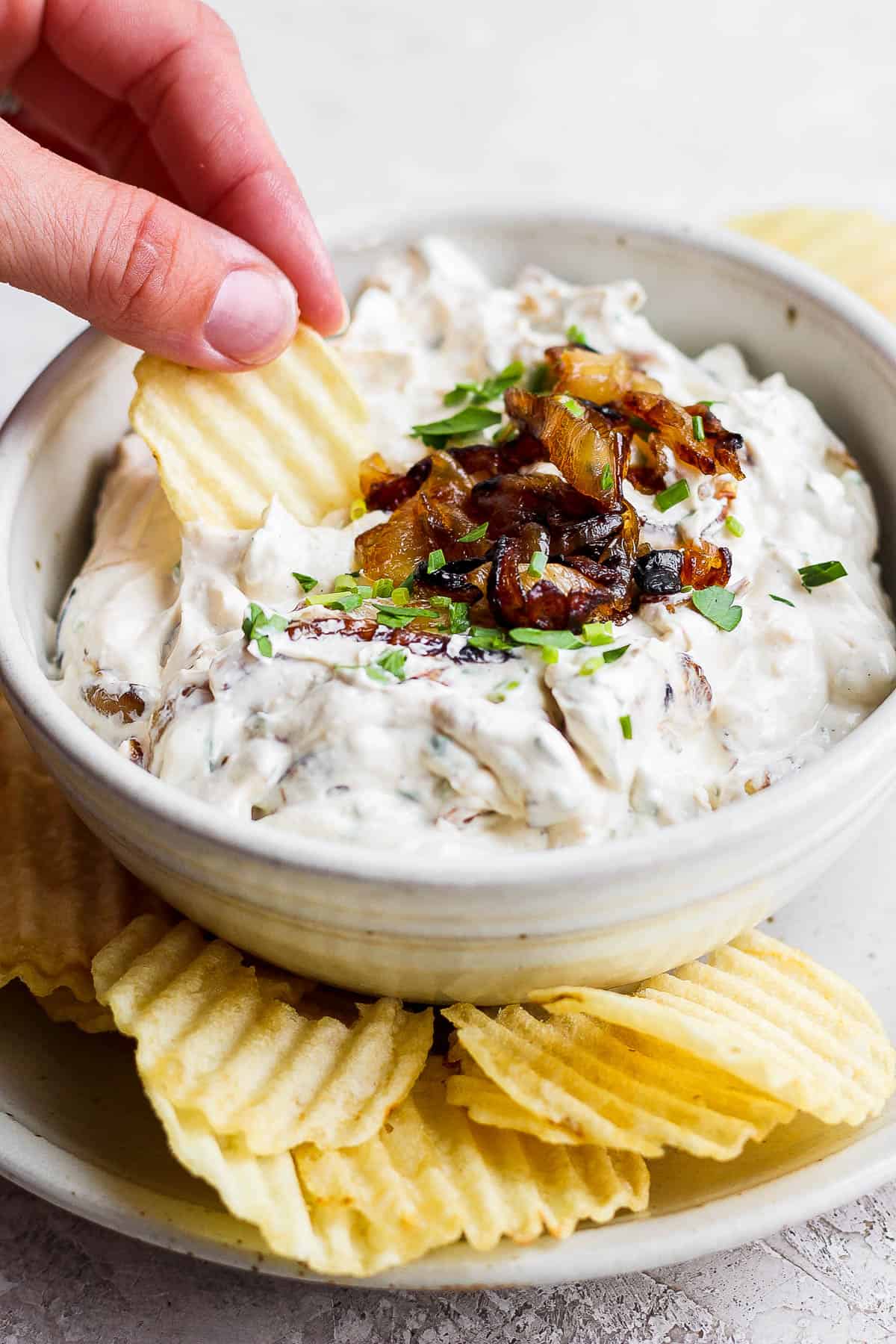 A hand scooping some dip with a wavy potato chip.