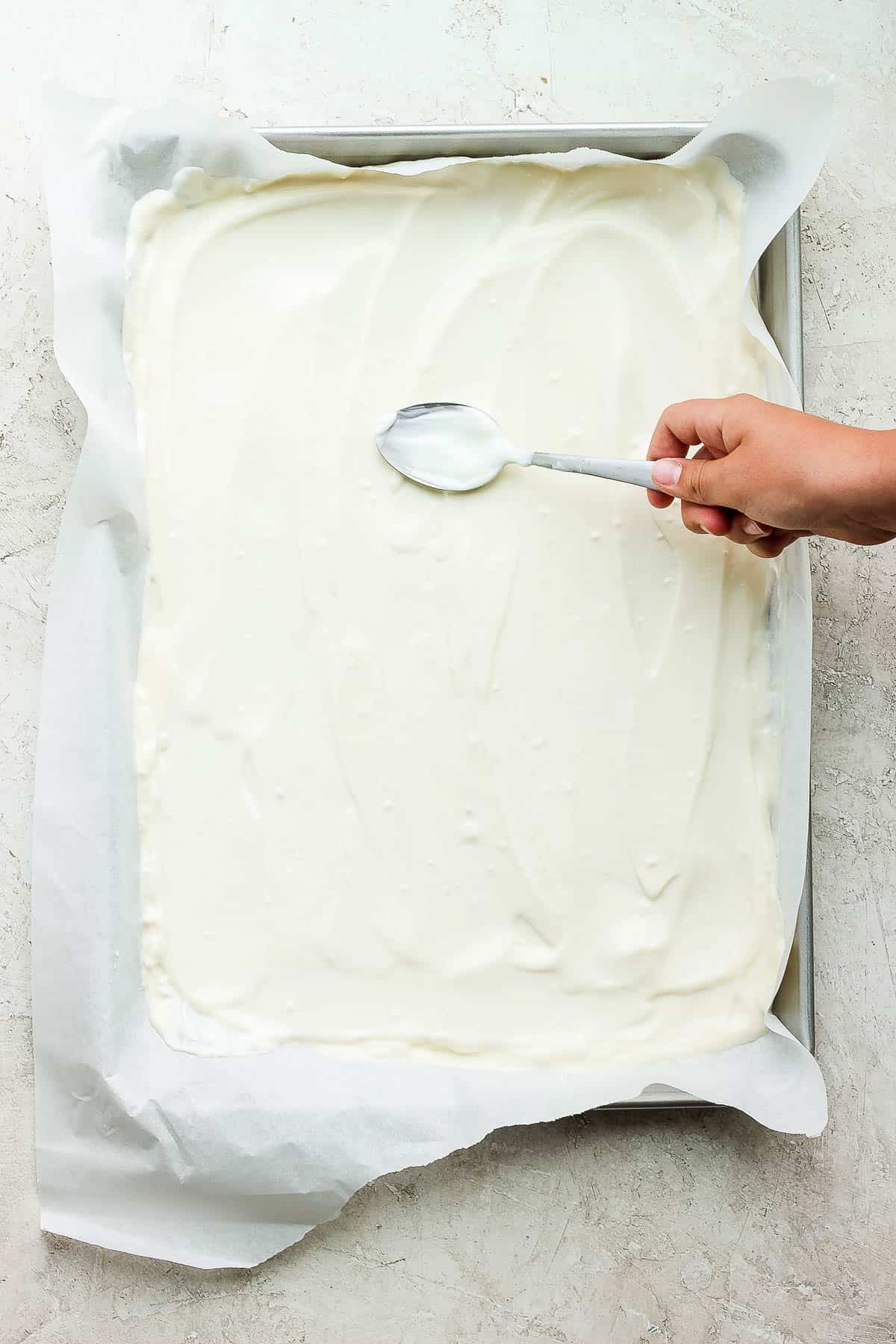 A spoon smoothing out yogurt on a parchment lined baking sheet.