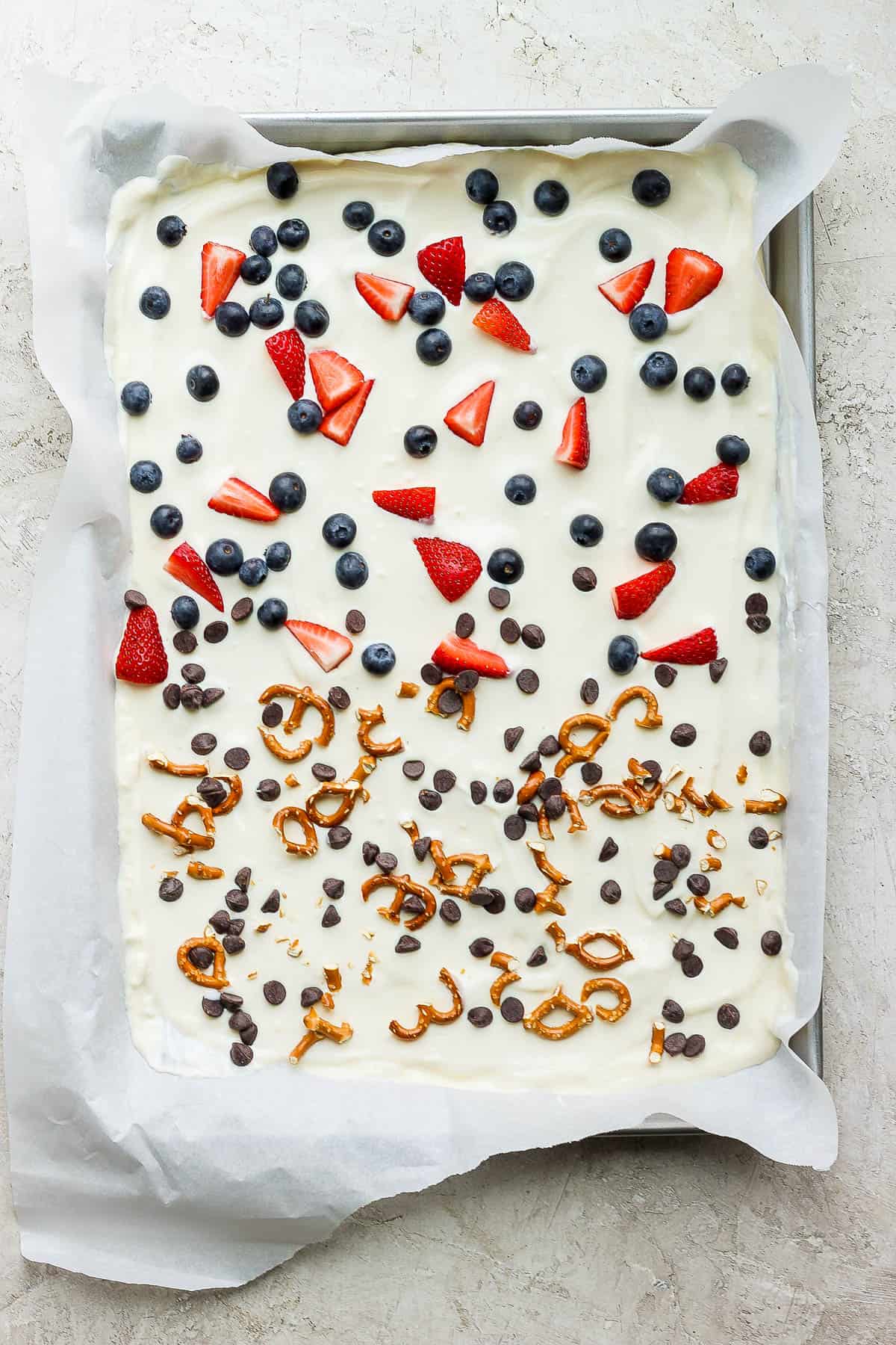 chopped strawberries, whole blueberries, crushed pretzels, and chocolate chips sprinkled on the yogurt in the pan.