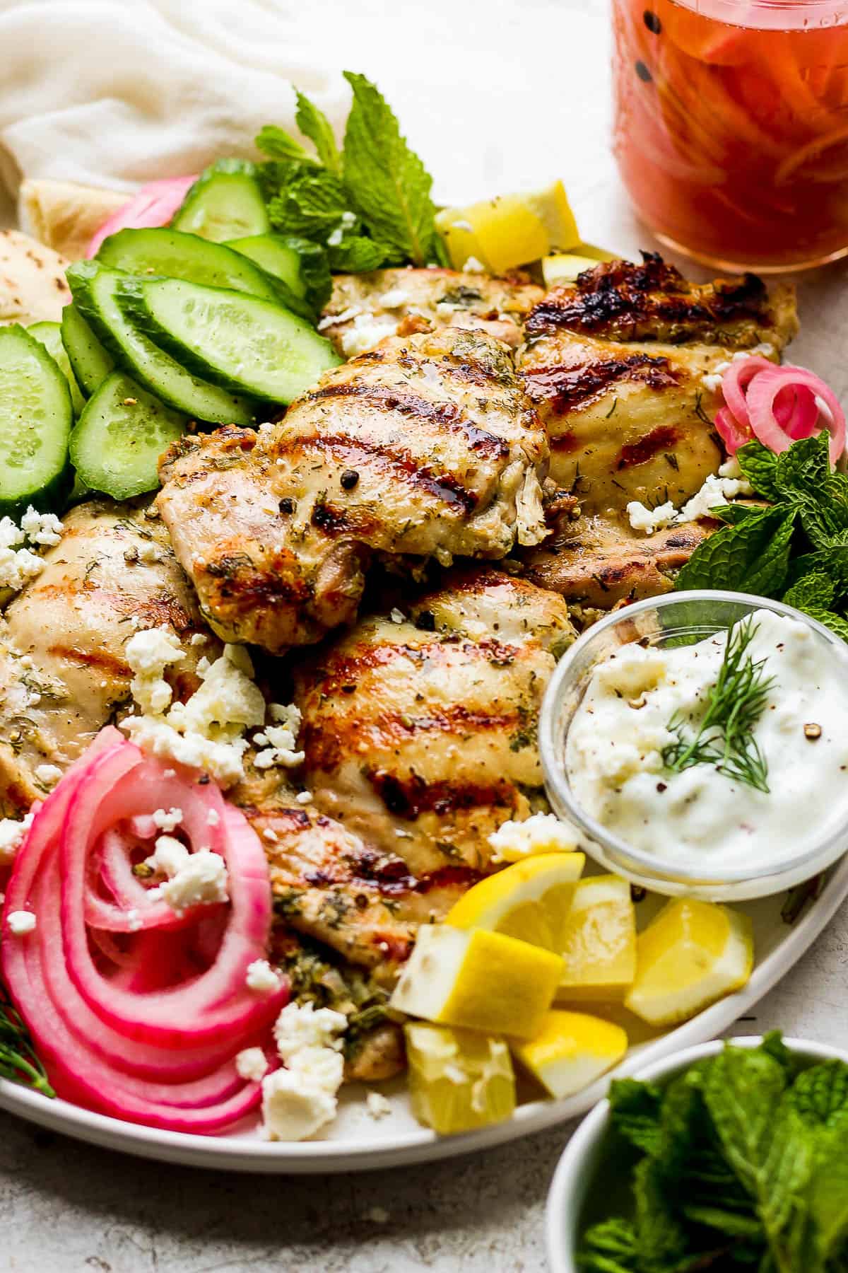 Grilled greek yogurt chicken garnished with cucumber wedges, pickled onion, tzatziki sauce, lemon wedges, crumbled feta, and fresh dill and mint.