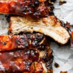 Close up shot of a rack of grilled ribs with bbq sauce with one rib flipped so the juicy cut side is up.