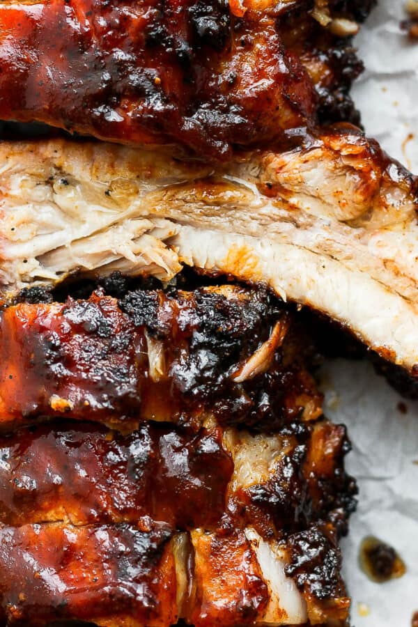 Close up shot of a rack of grilled ribs with bbq sauce with one rib flipped so the juicy cut side is up.