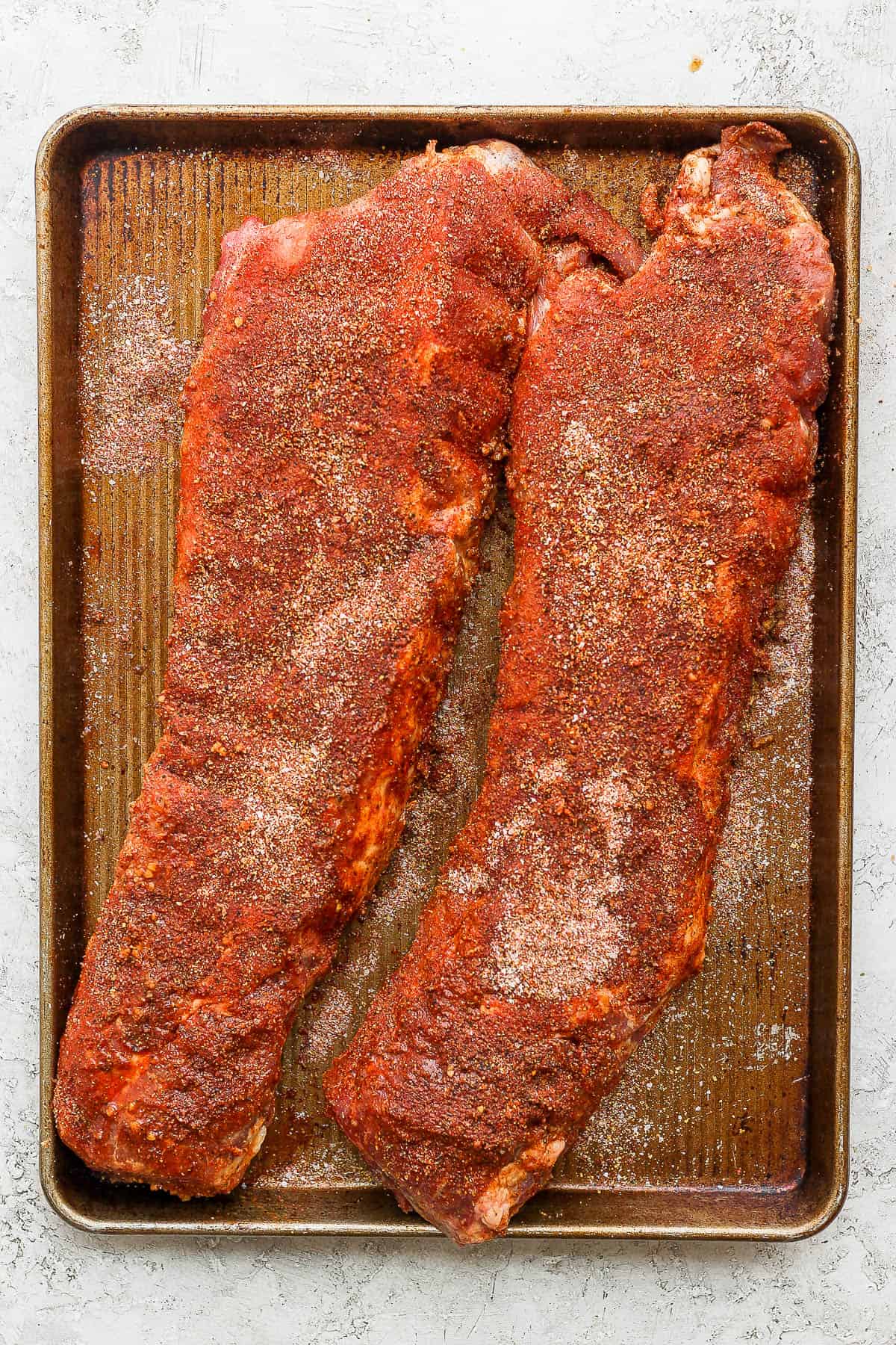 Marinated ribs on a baking sheet with the dry rub spices rubbed all over them.