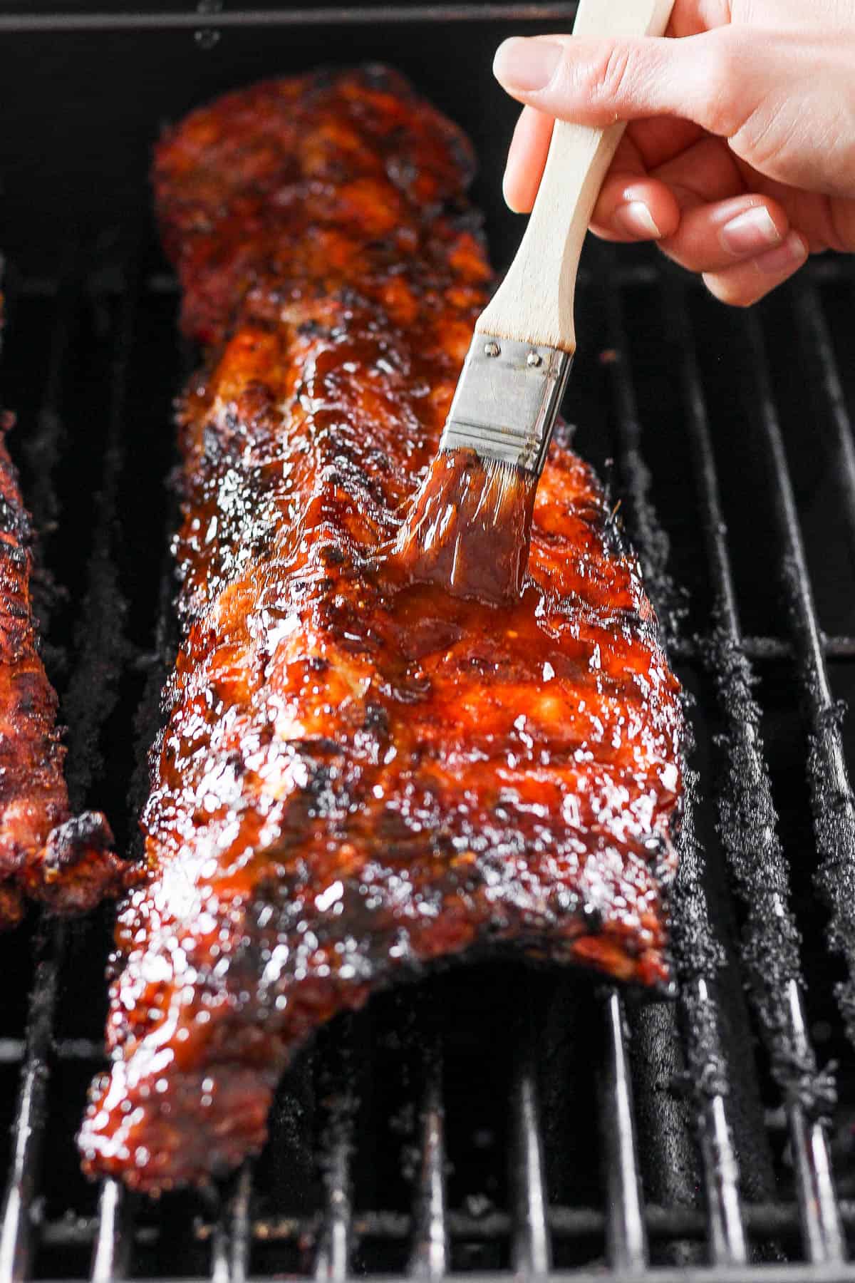 BBQ sauce being brushed on the ribs while they are finishing on the grill.