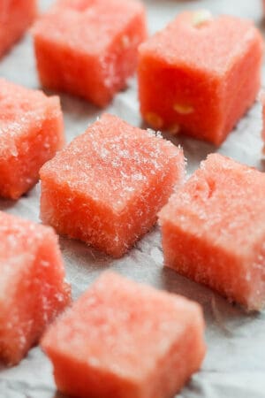 Several pieces of frozen watermelon on a parchment-lined baking sheet.
