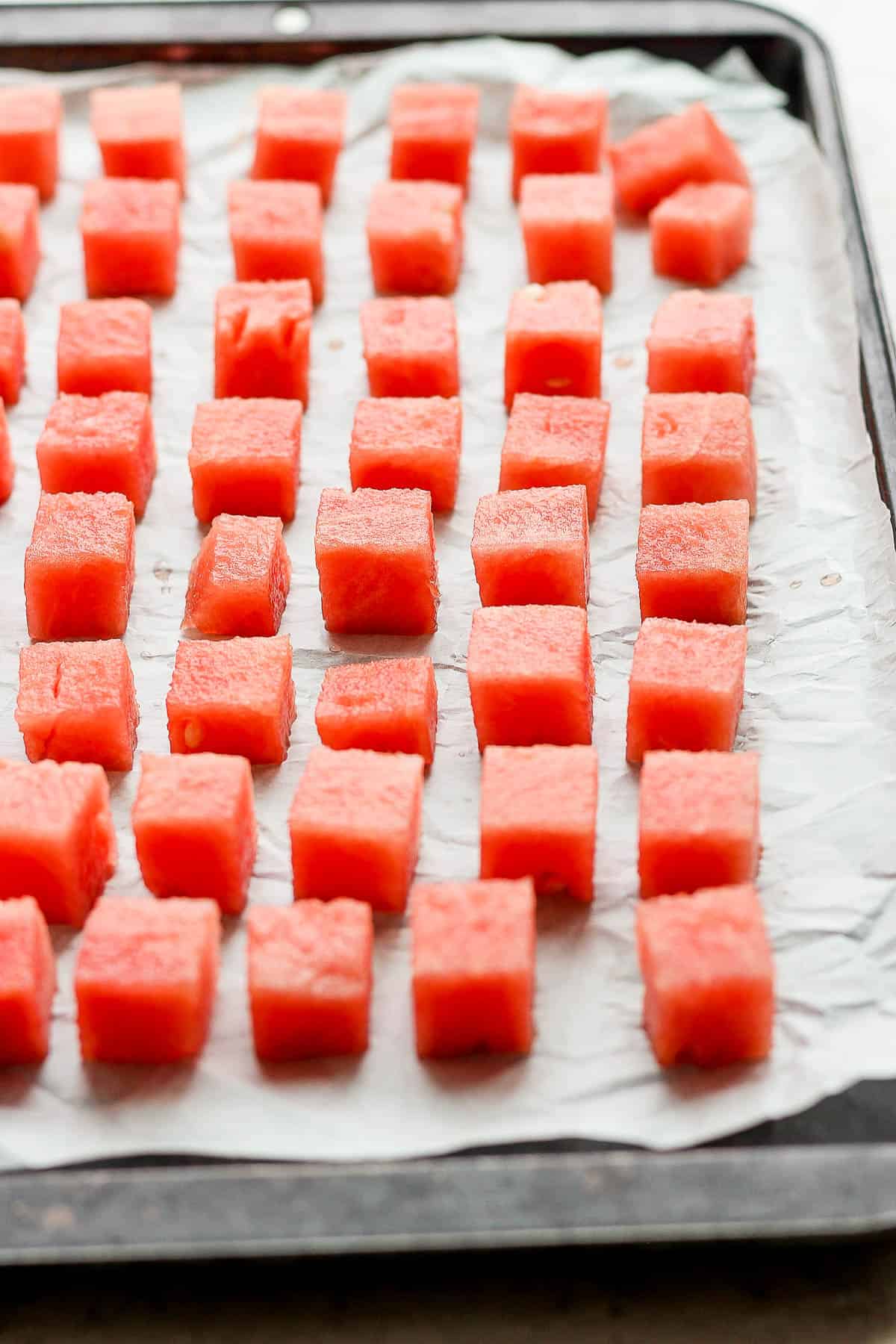 Large chunks of fresh watermelon on a parchment-lined baking sheet.