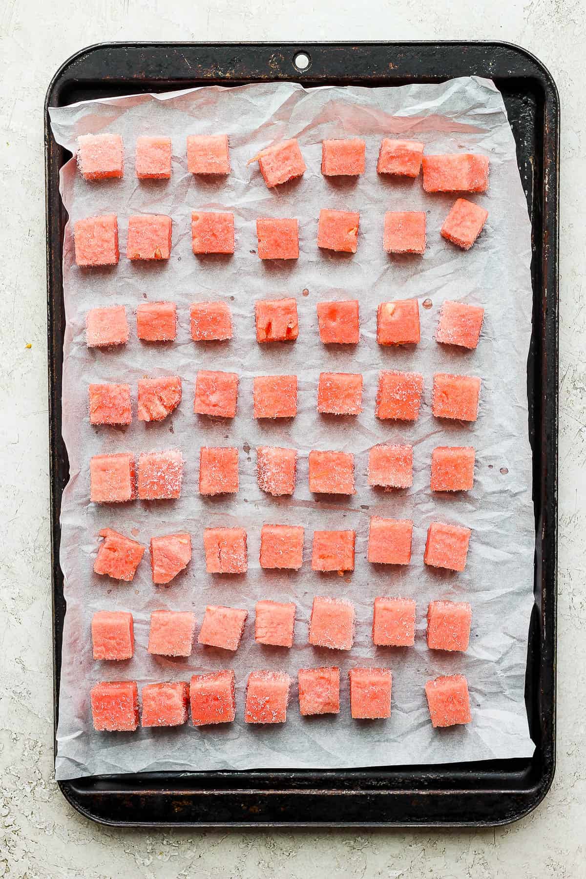Frozen chunks of watermelon on a parchment-lined baking sheet.