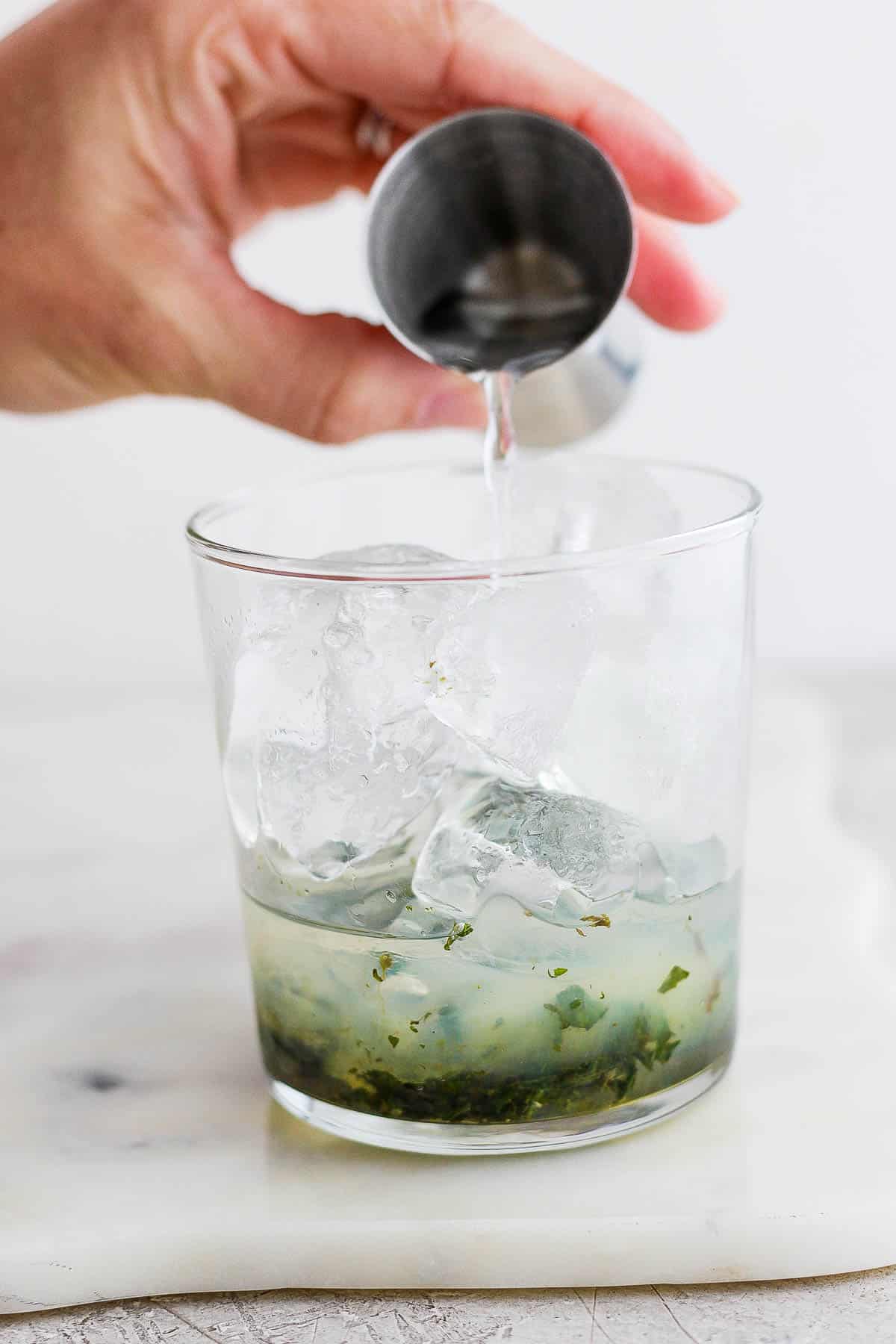 White rum being poured over ice in the glass with the muddled mint.
