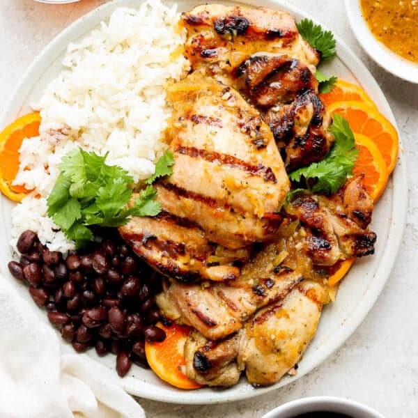 Top down shot of a plate of mojo chicken, rice and seasoned black beans with cilantro and orange slices.