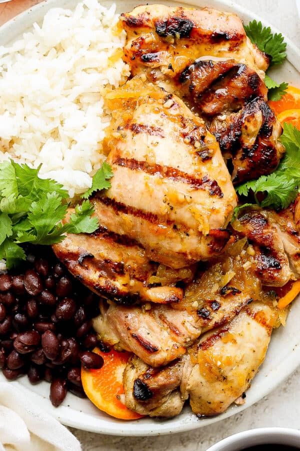 Top down shot of a plate of mojo chicken, rice and seasoned black beans with cilantro and orange slices.