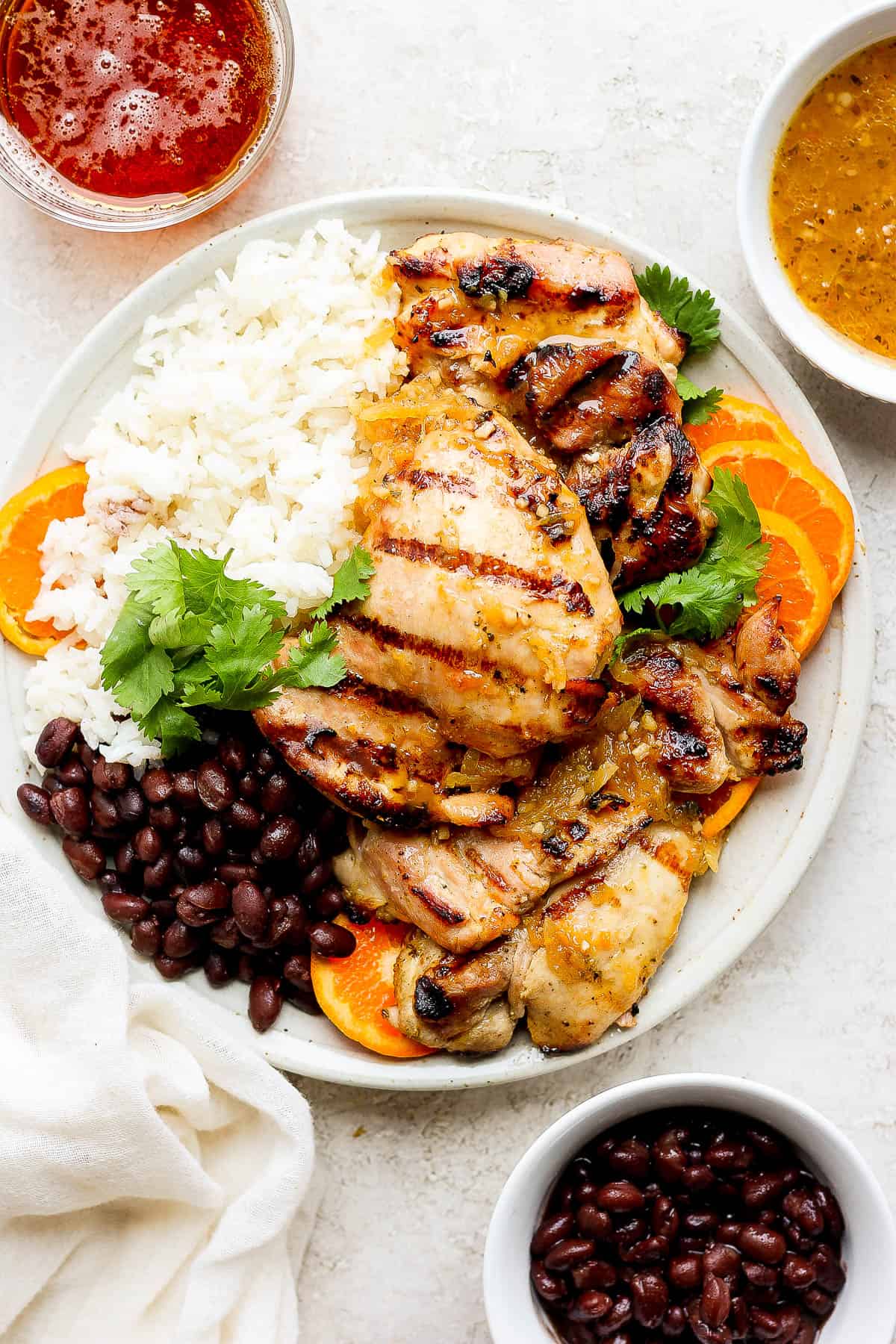 A plate of mojo chicken, rice, and seasoned black beans garnished with orange slices and cilantro.