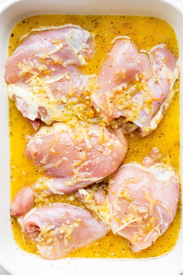 Top down shot of a pan filled with chicken thighs covered in a mojo marinade.