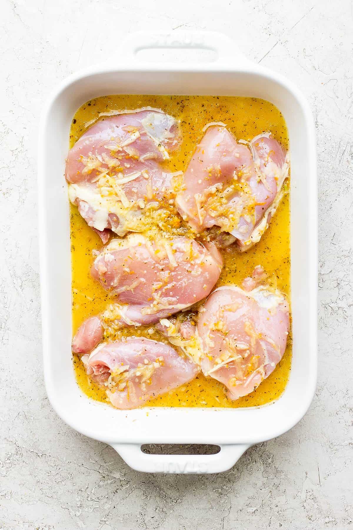 Mojo marinade poured over chicken thighs in a white baking dish.