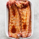 Top down shot of a 2 racks of ribs in a marinade sitting in a white baking dish.