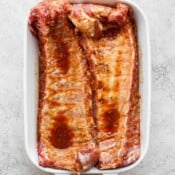 Top down shot of a 2 racks of ribs in a marinade sitting in a white baking dish.