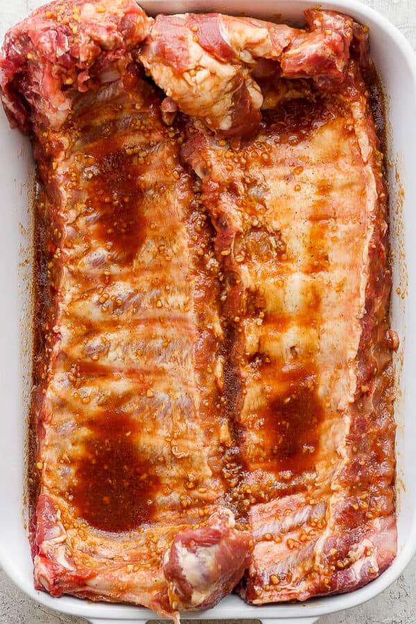 Two racks of ribs in a marinade sitting in a white baking dish.