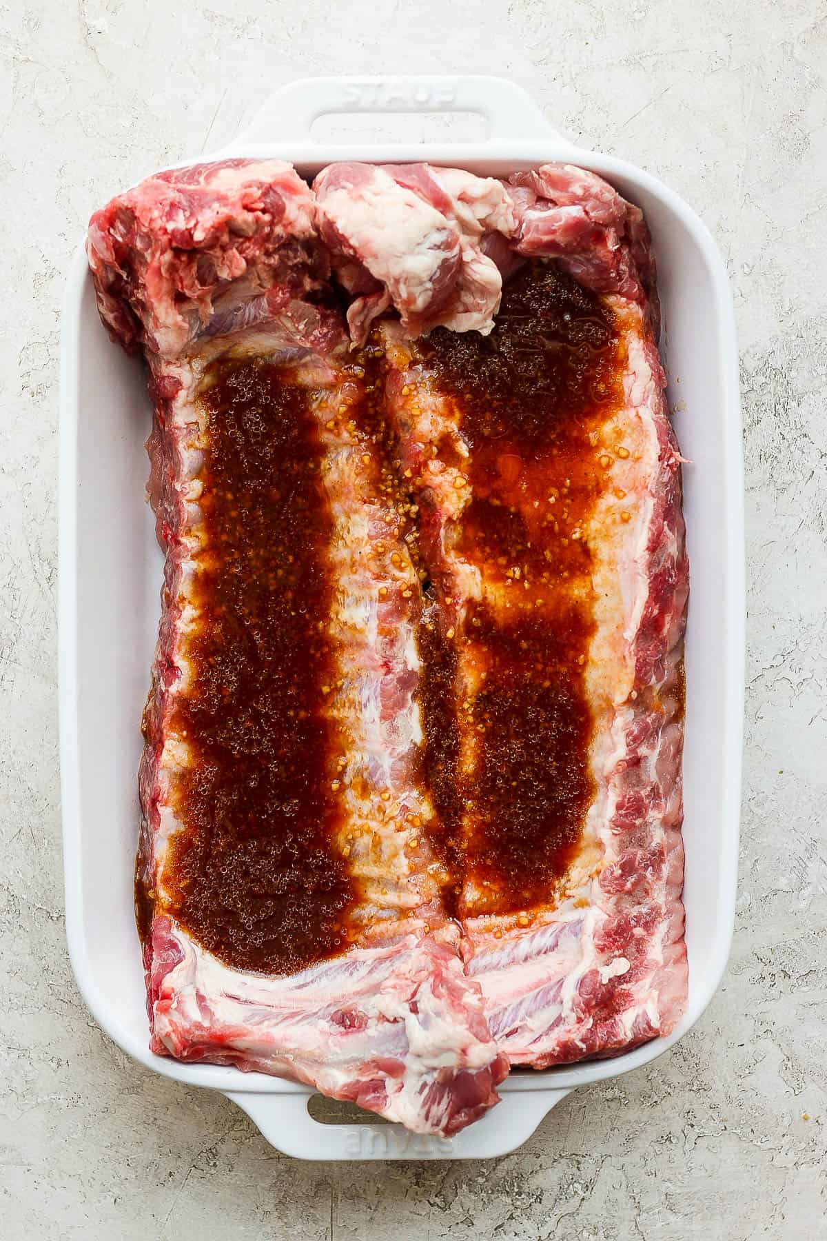 Rib marinade poured over two racks of ribs in a white baking dish.