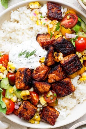 Top down shot of a bowl with blackened salmon bites, dill sauce and grilled corn salad over rice.