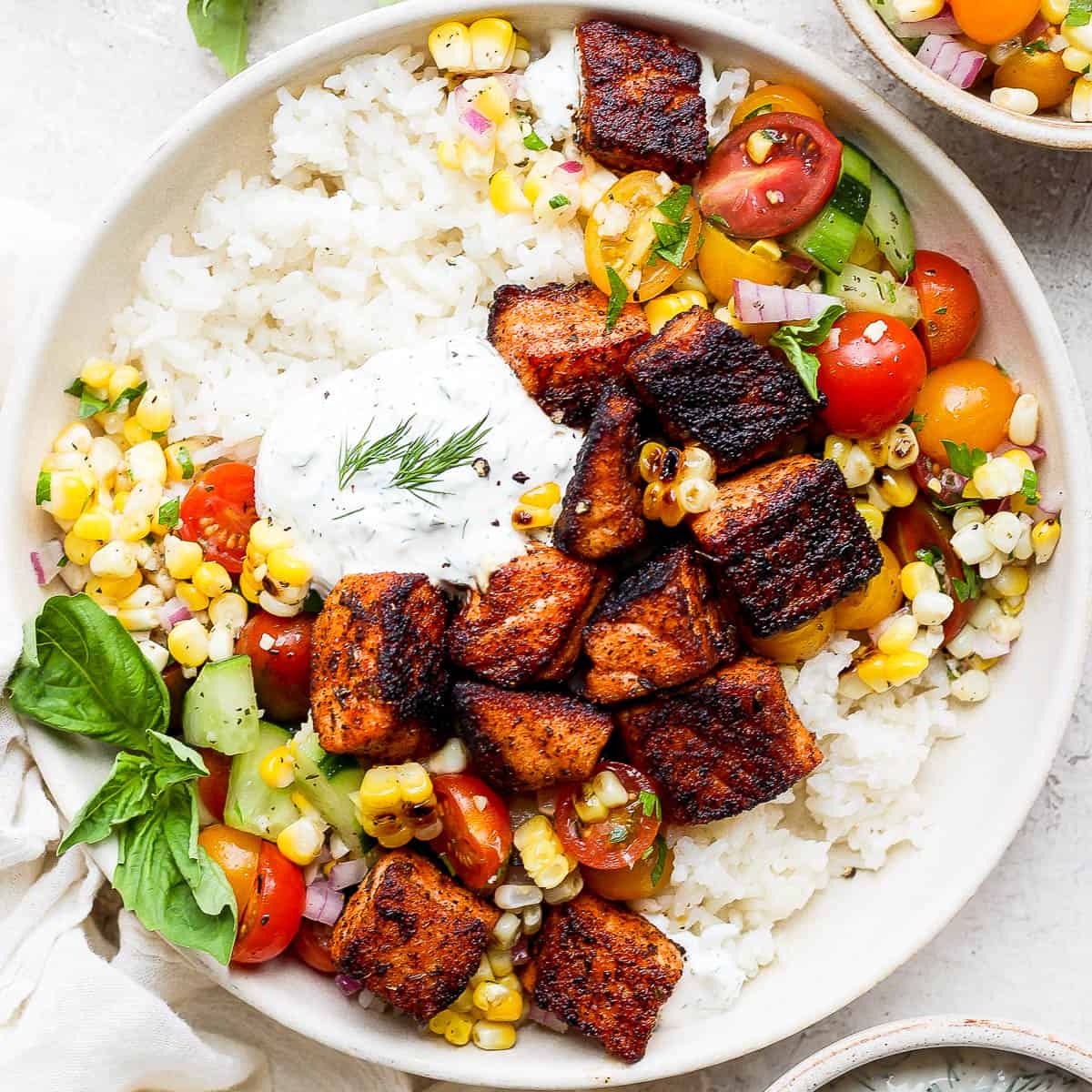 Top down shot of a bowl with blackened salmon bites, dill sauce and grilled corn salad over rice.