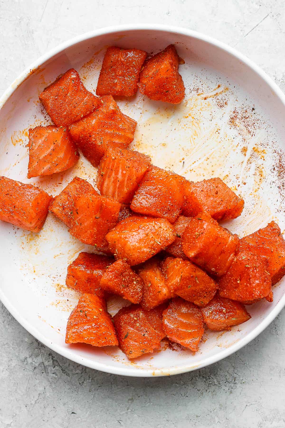 Raw salmon chunks in a bowl with blackened seasoning.
