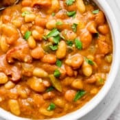 Top down shot of a bowl of slow cooker baked beans with some parsley garnish.