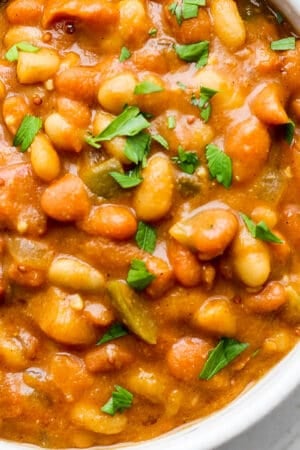 Top down shot of a bowl of slow cooker baked beans with some parsley garnish.