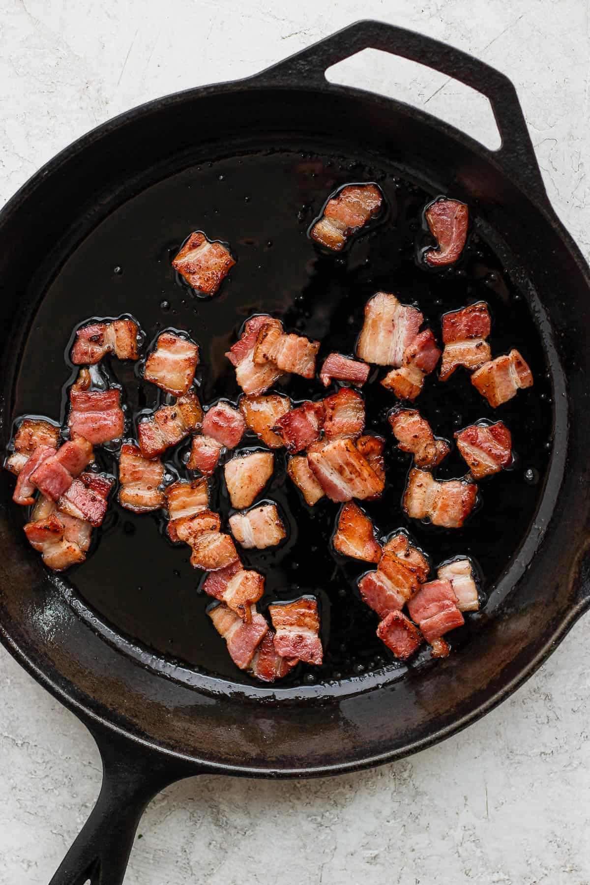 Pieces of bacon cooking in a cast iron skillet.