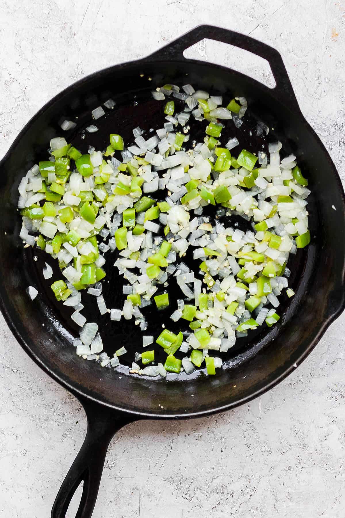 Onion, garlic, and green bell pepper cooking in the skillet after the bacon was removed.