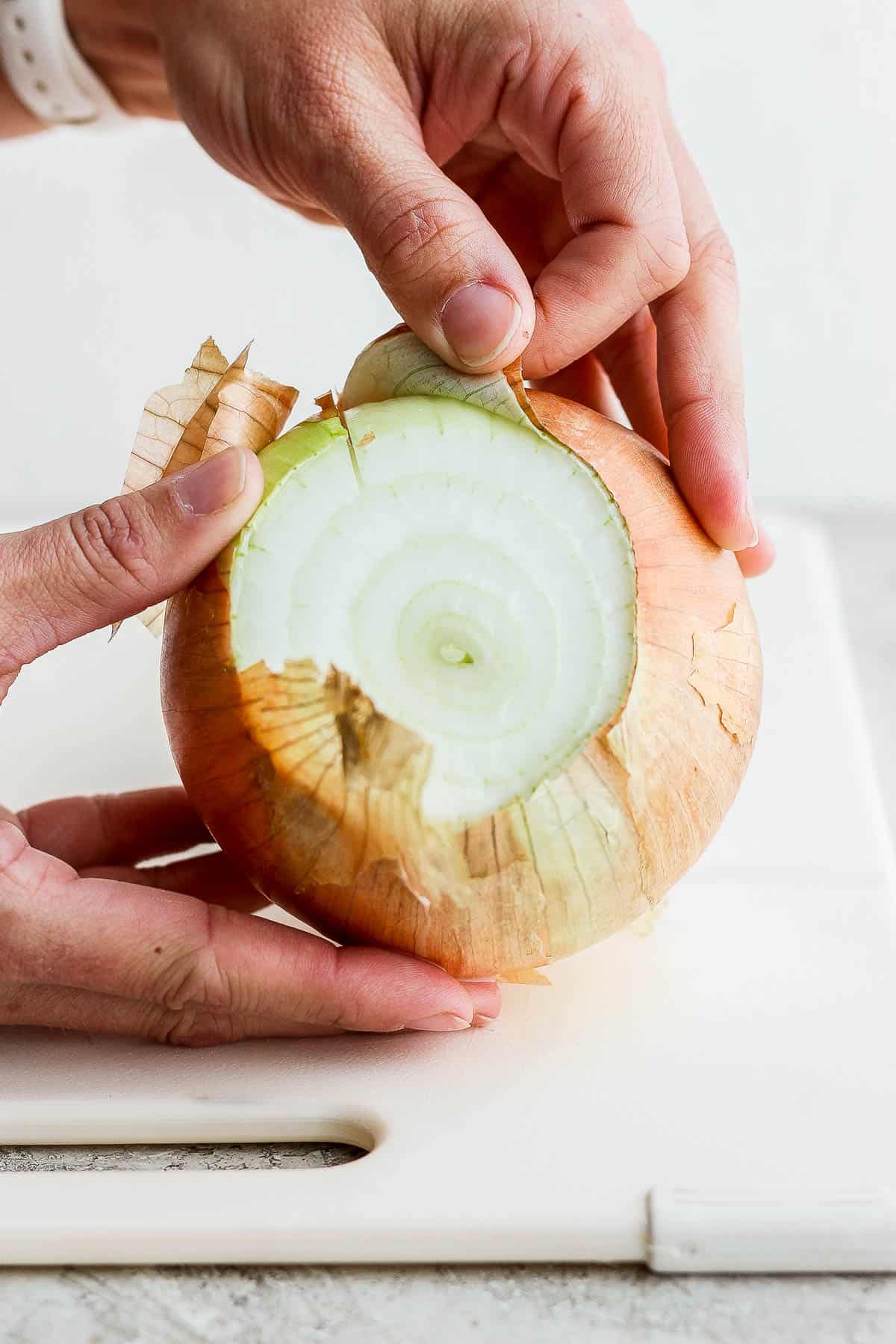 Two hands peeling the outside off an onion.