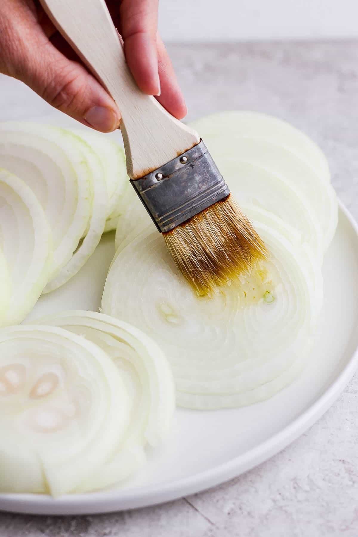 Onion slices on a plate being brushed with olive oil.