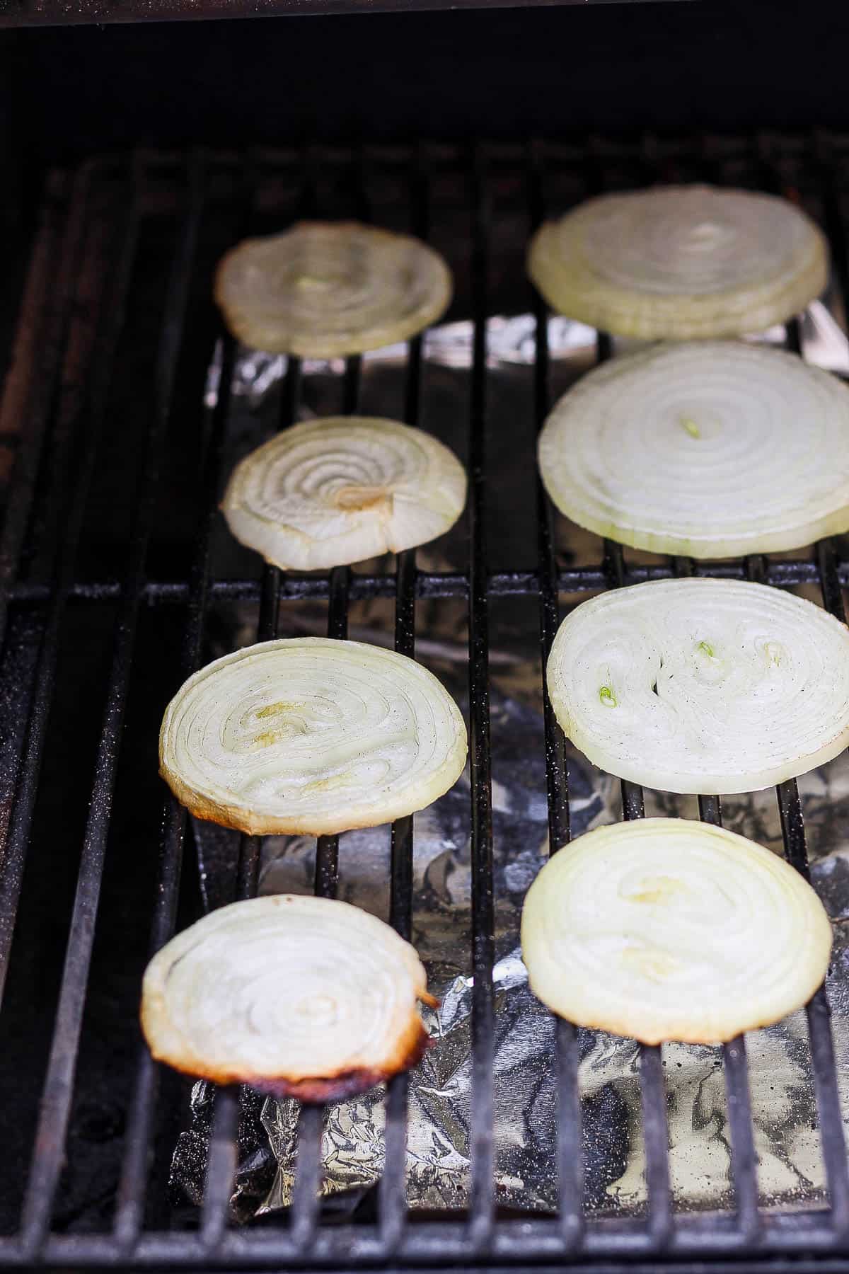 Onion slices on the grates of a smoker.
