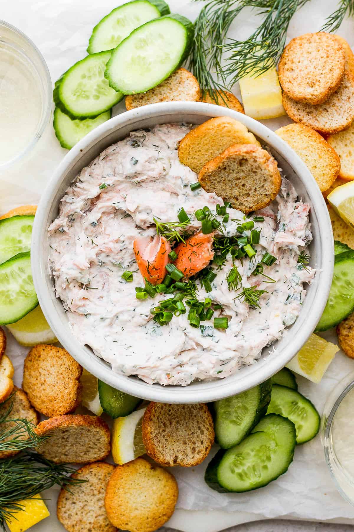 All of the ingredients mixed together in a bowl garnished with crostini crackers, cucumber wedges, and lemon wedges.