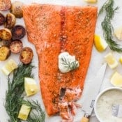 A piece of smoked salmon on a piece of parchment with a dollop of tartar sauce on top and potatoes and dill around it.