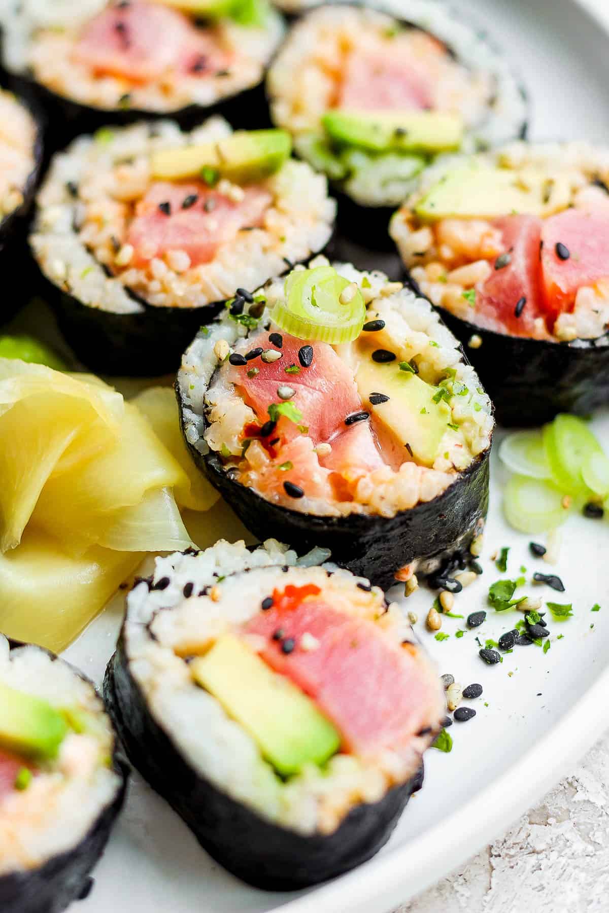 Fully garnished pieces of a spicy tuna roll on a white plate.