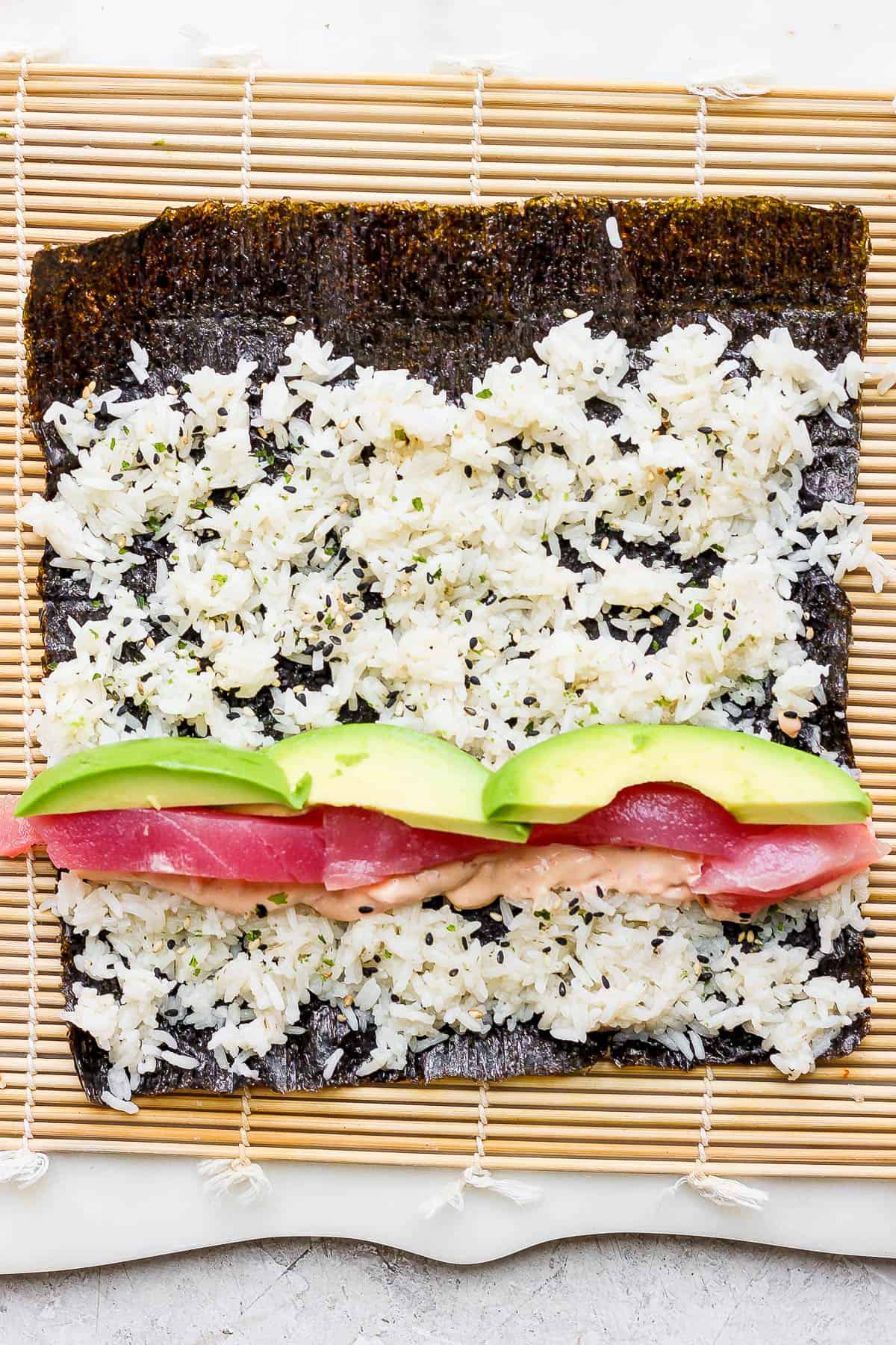 A nori sheet on a bamboo sheet with rice spread on top and filling ingredients added.