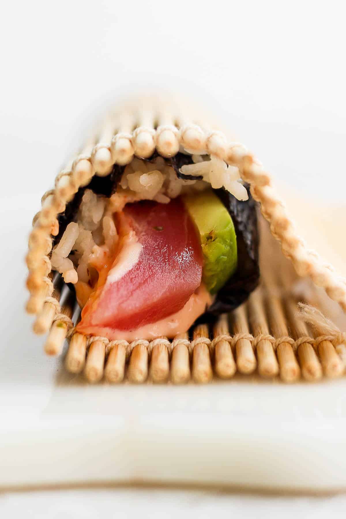 A spicy tuna roll all rolled up in a bamboo sheet.