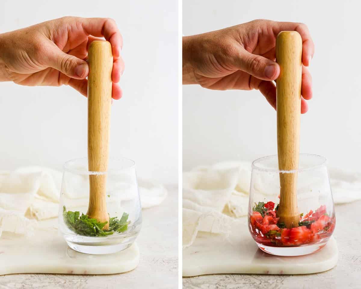 A hand muddling mint leaves into the bottom of the sugar rimmed glass.  A hand muddling strawberries with the mint into the sugar rimmed glass.