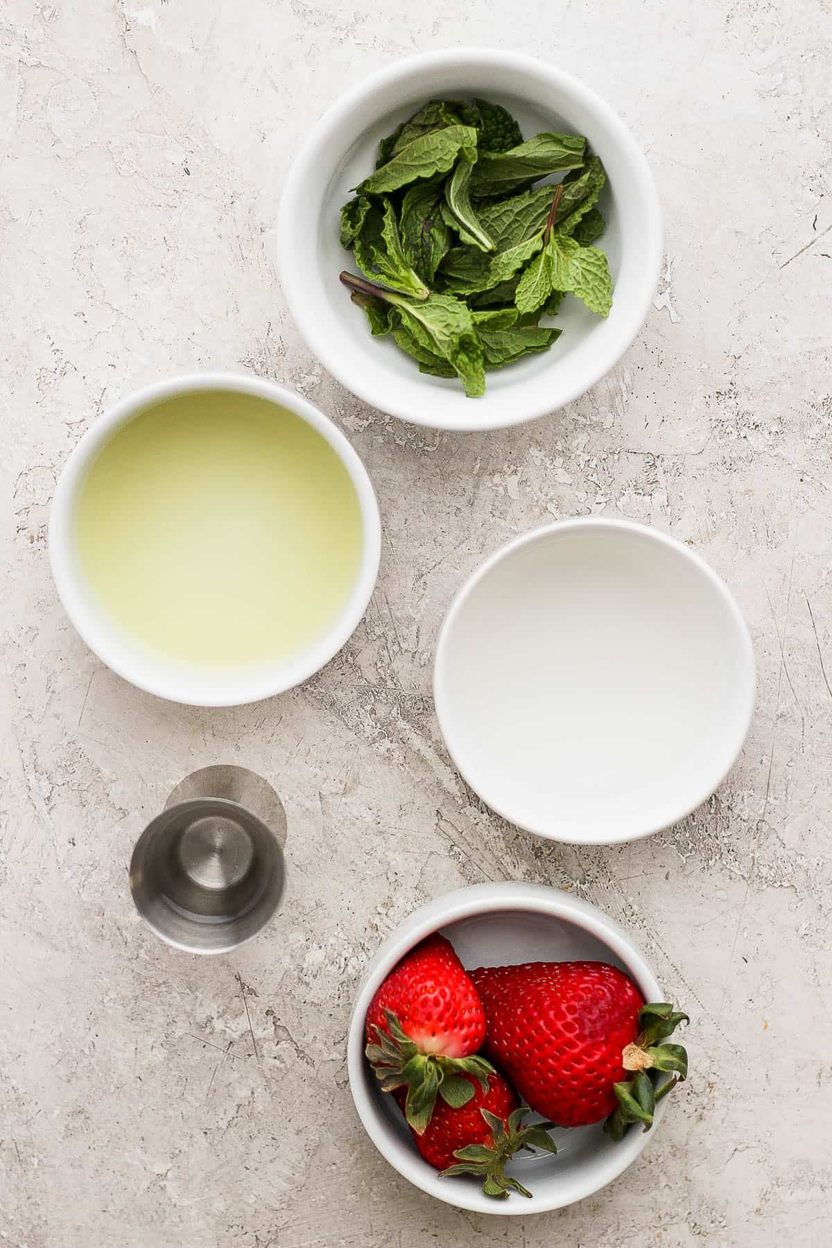 Individual ingredient bowls, each with the following: three whole strawberries, fresh mint leaves, white rum, lime juice, and simple syrup.
