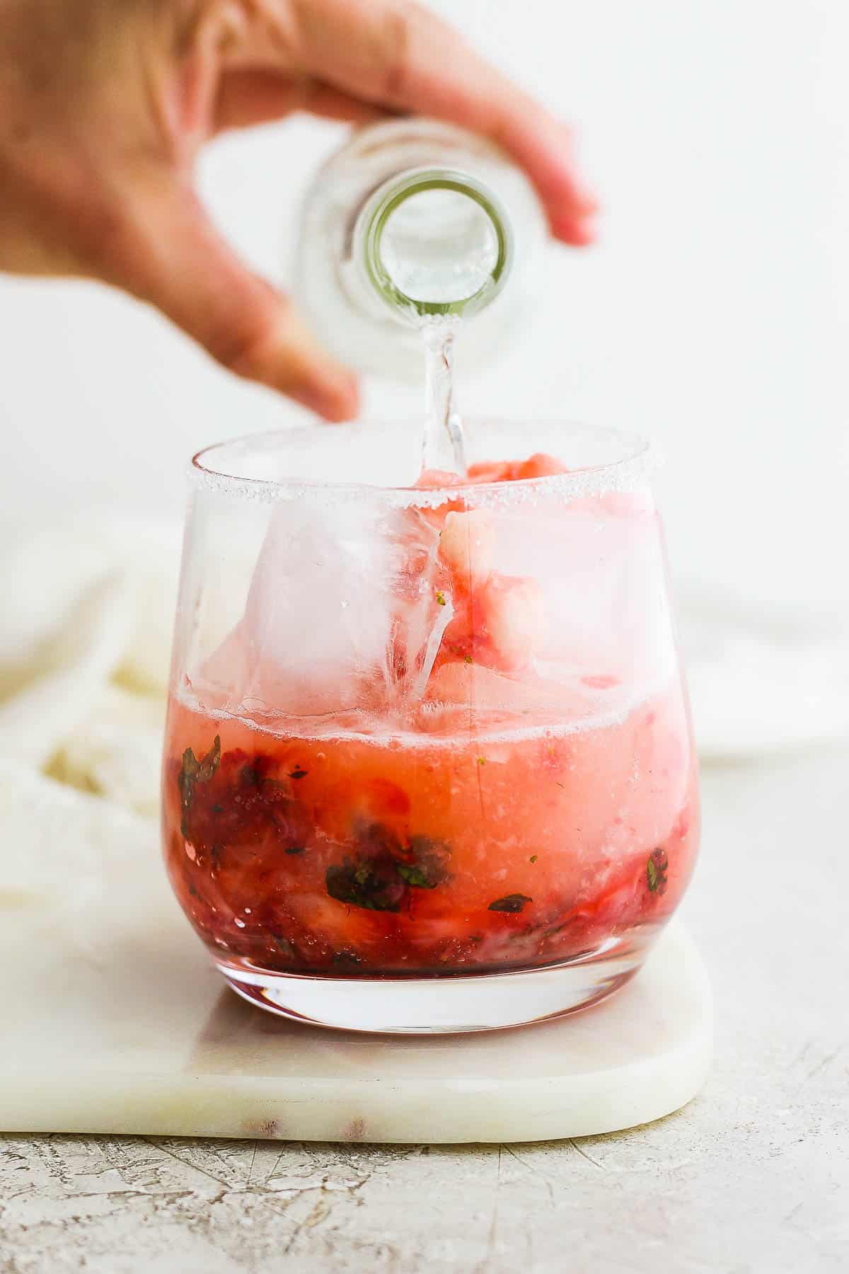 The strawberry mixture in the sugar rimmed glass being topped with tonic water.