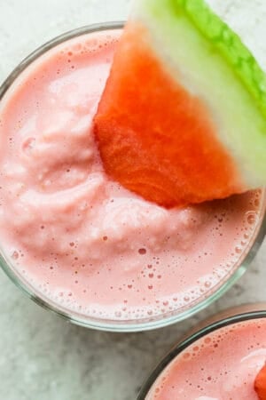 Top down shot of two glasses of watermelon smoothie with small wedges of watermelon sticking out.