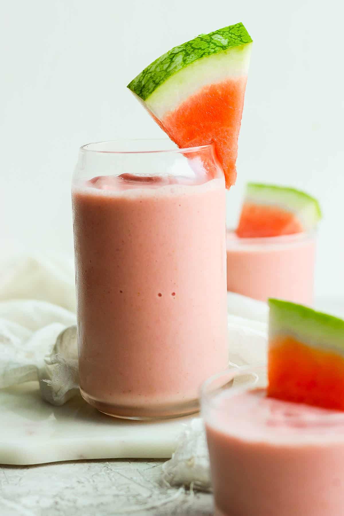 A frozen watermelon smoothie with a wedge of fresh watermelon on the side of the glass.
