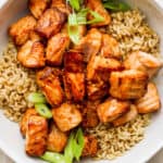 Bowl of brown rice with sliced green onions and cooked air fryer salmon bites.