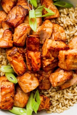 Bowl of brown rice with sliced green onions and cooked air fryer salmon bites.