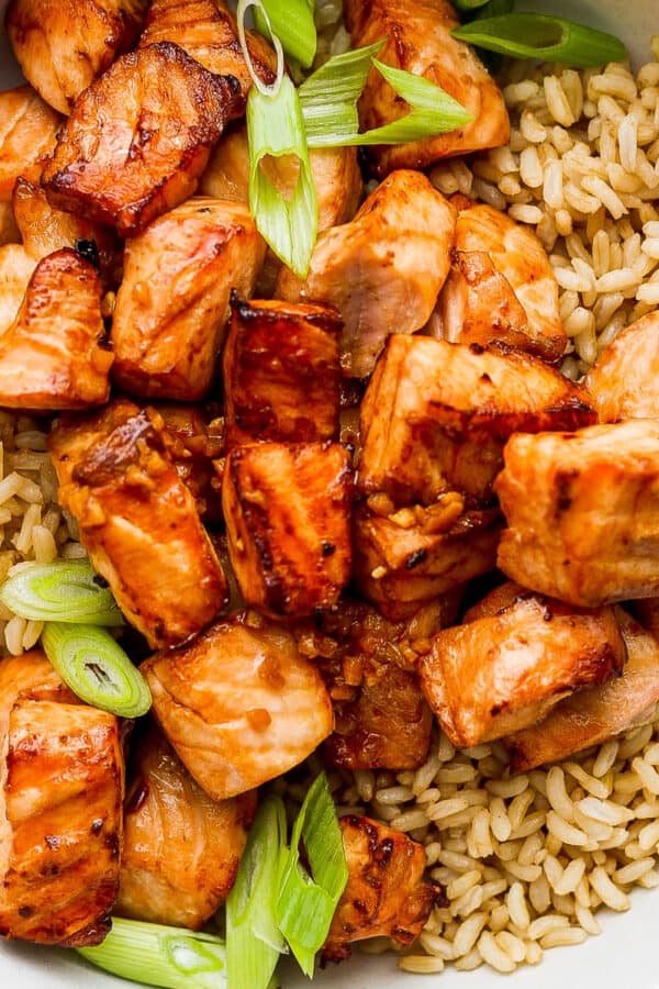 Bowl of brown rice with sliced green onions and cooked air fryer salmon bites.