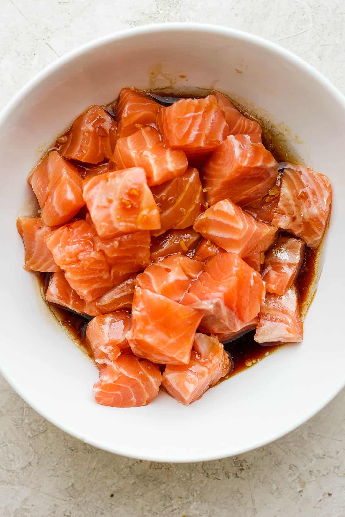 Fresh salmon bites in a white bowl with the marinade on top.