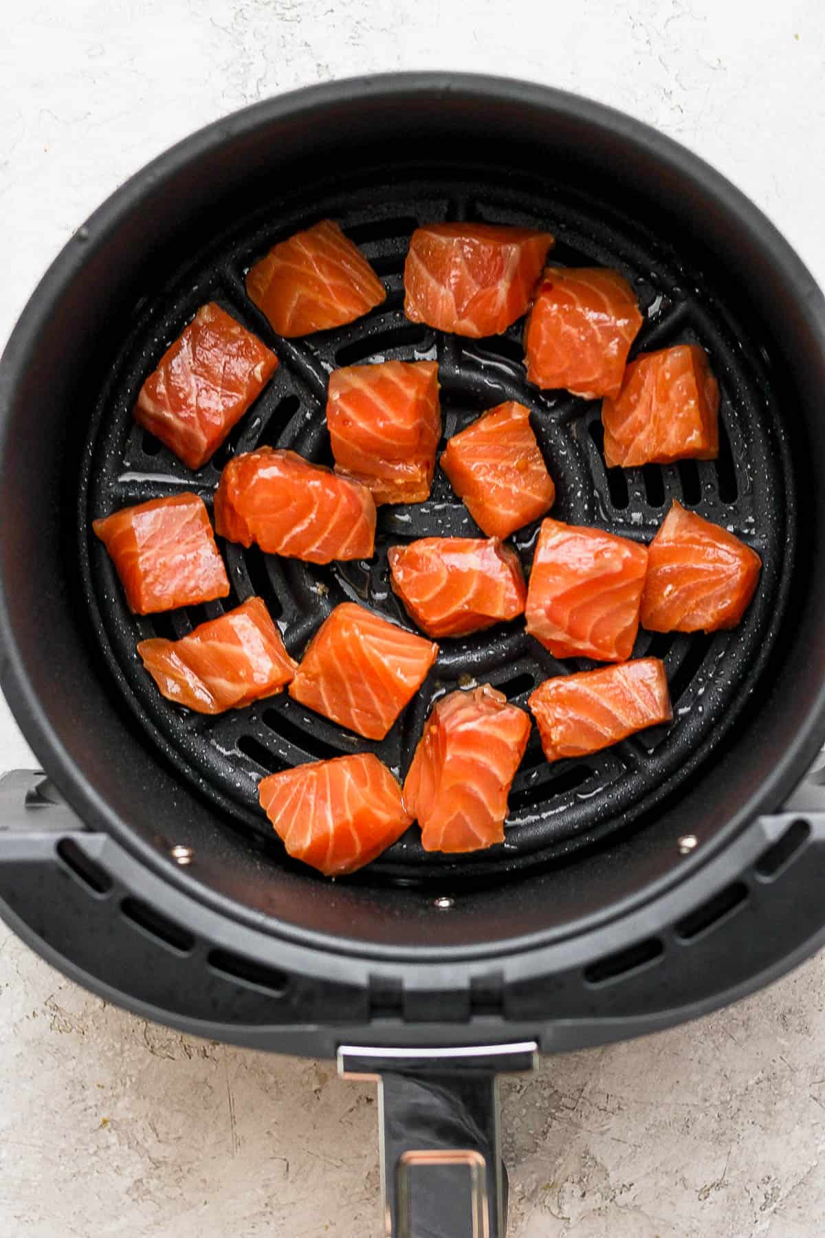 Marinated salmon bites in the air fryer basket before cooking.