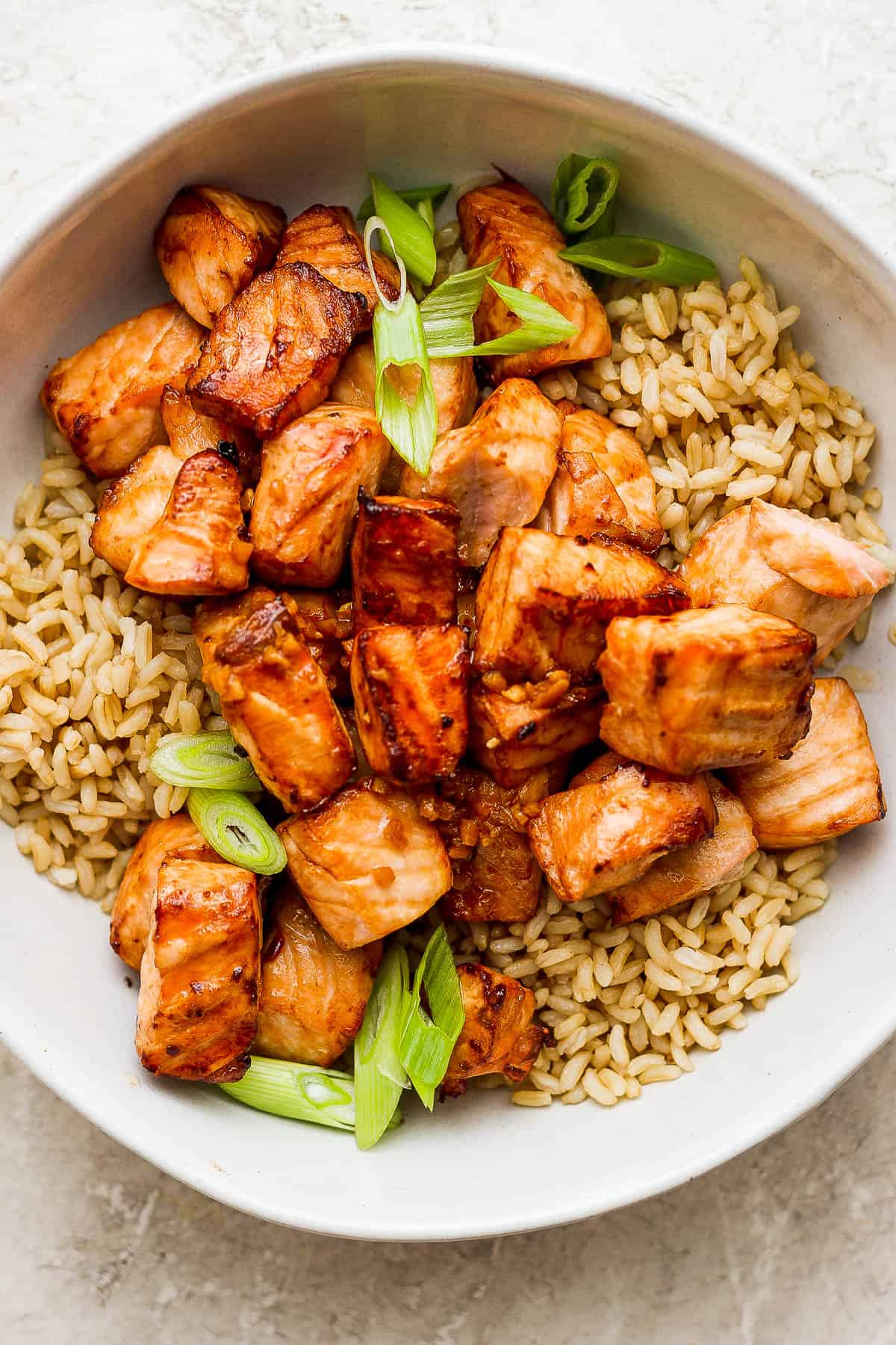 Air fryer salmon bites in a bowl with rice and chopped green onions.
